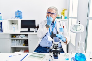 Senior caucasian man working at scientist laboratory looking stressed and nervous with hands on...