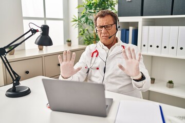 Senior doctor man working on online appointment moving away hands palms showing refusal and denial with afraid and disgusting expression. stop and forbidden.