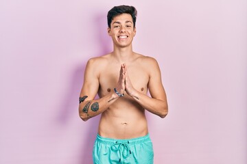 Fototapeta premium Young hispanic man wearing swimwear shirtless praying with hands together asking for forgiveness smiling confident.