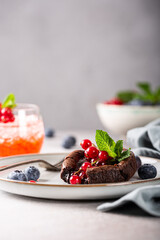 Warm chocolate Lava Cake with bite taken out of molten center, red currants, bleuberry and mint leaves on gray background, copy space