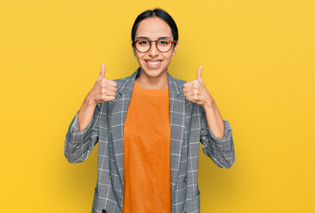 Young hispanic girl wearing business jacket and glasses success sign doing positive gesture with...