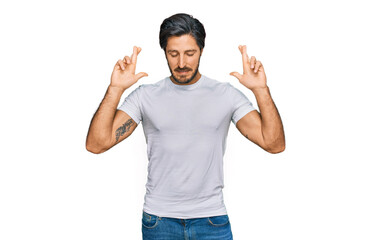 Fototapeta premium Young hispanic man wearing casual white t shirt gesturing finger crossed smiling with hope and eyes closed. luck and superstitious concept.