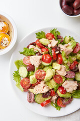 Salad with tuna, lettuce, cucumbers, tomatoes, olives and avocados in white plate on the table
