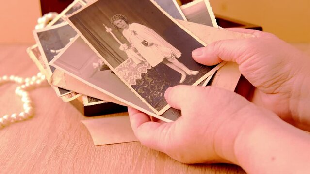 female hands are sorting dear to heart memorabilia in an old wooden box, stack of retro photos, vintage photographs of 1960, concept of family tree, genealogy, childhood memories, home archive
