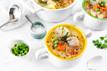 Soup with meatballs, cauliflower, baby peas, carrots and cream on a white background.