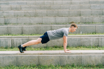 Fototapeta premium Young man has fitness workout. Male athlete does abs exercise, sport and training outdoor and stands in plank. People sport and healthy lifestyle concept.