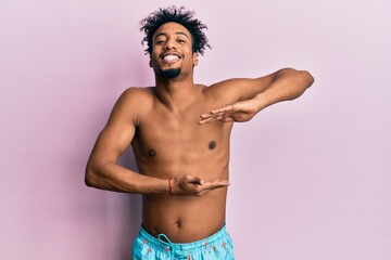 Fototapeta premium Young african american man with beard wearing swimsuit gesturing with hands showing big and large size sign, measure symbol. smiling looking at the camera. measuring concept.