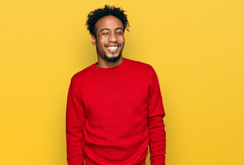 Young african american man with beard wearing casual winter sweater winking looking at the camera...