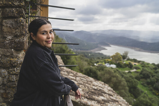 Photo Of A Caucasian Woman Leaning Over Balcony Railing And Looking At The Camera