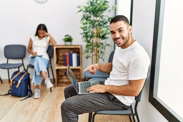 Fototapeta premium Young people sitting at waiting room working with laptop smiling happy pointing with hand and finger
