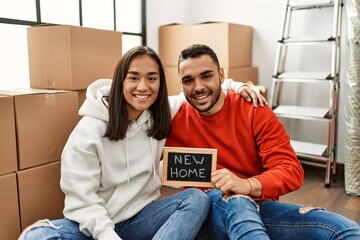 Young latin couple smiling happy holding blackboard with new home message.