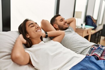 Young hispanic couple relaxing with hands on head lying in bed at home.