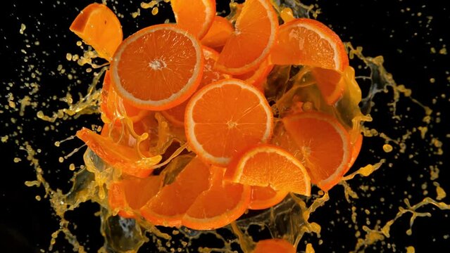 Super slow motion shot of rotating exploded orange slices with splashing juice on black at 1000fps.