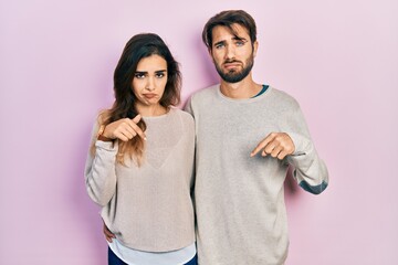 Young hispanic couple wearing casual clothes pointing down looking sad and upset, indicating direction with fingers, unhappy and depressed.