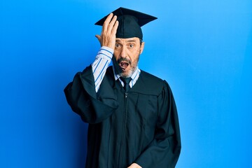 Middle age hispanic man wearing graduation cap and ceremony robe surprised with hand on head for mistake, remember error. forgot, bad memory concept.
