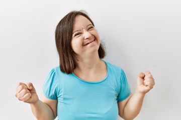 Young down syndrome woman standing over isolated background very happy and excited doing winner gesture with arms raised, smiling and screaming for success. celebration concept.