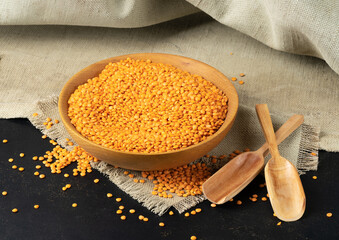 A bowl of red lentils on a rough napkin with a dark background.