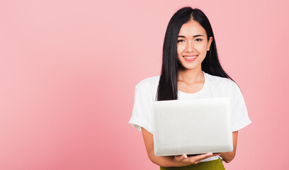 Fototapeta premium Portrait of happy Asian beautiful young woman confident smiling face holding using laptop computer looking to camera, studio shot isolated on pink background, with copy space