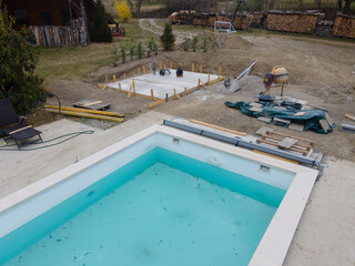 Drone shot of pool construction site with concrete pad for heat pump and pool house in garden in...