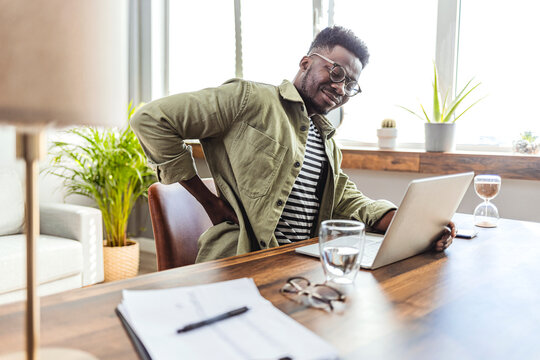 Shot of African American businessman suffering from back pain while trying to work in the office.  Businessman experiencing back pain while working at his desk