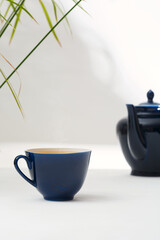 Tea in a dark blue ceramic cup and a teapot on a white table.