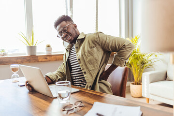 Male businessman who suffers back pain from working from home. Shot of a young businessman...