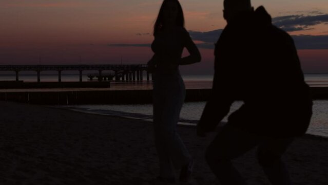 couple silhouette on beach in sunset evening, man taking photo, young female woman posing him. romantic mouth relationships, dating, love emotions, romantic evening on coastline, 