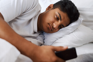Still no text back from her. Shot of a young man using his cellphone while lying on his bed.