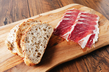 Premium Spanish dry cured ham on a wooden board and wooden background and a slice of bread . Top...
