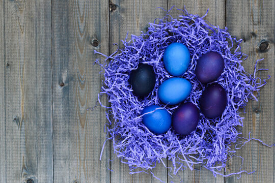 On a wooden rustic table, a flat lay top view of paper shaving fillers on which bright eggs were laid for the Easter holiday painted in blue and very peri colors, copy space. - Powered by Adobe
