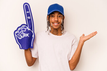 Young sports fan African American man isolated on white background showing a copy space on a palm and holding another hand on waist.