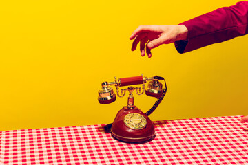 Retro objects, pop art photography. Female hand holding handset of vintage phone isolated on bright...