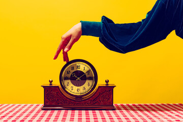 Retro things, pop art photography. Female hand touching vintage clock isolated on bright yellow background. Vintage, retro fashion style