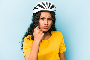 Young hispanic woman wearing a helmet bike isolated on blue background showing fist to camera, aggressive facial expression.