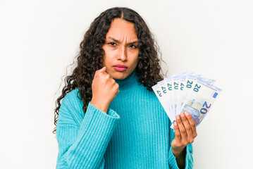 Young hispanic woman holding banknotes isolated on white background showing fist to camera, aggressive facial expression.