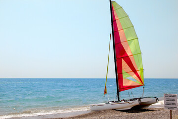 a yacht with a raised sail is standing on the sand by the water