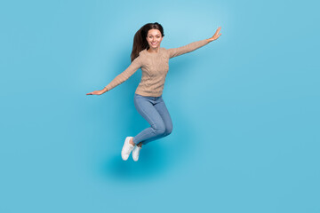 Fototapeta na wymiar Photo of cheerful nice lady jump raise hands wear beige sweater jeans sneakers isolated blue color background