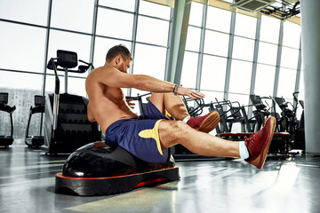 Fototapeta na wymiar Handsome muscular men works out on functional training soft platform on a background of gym.