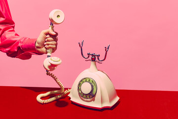 Pop art photography. Retro objects, gadgets. Female hand holding handset of vintage phone isolated on pink and red background. Vintage, retro fashion style