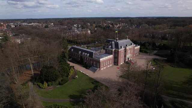 Ascending aerial of Slot Zeist castle with the moated manor surrounded by green park and urban landscape in the background. Dutch stately venue seen from above.
