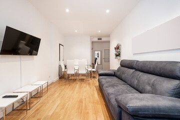 Living room with three-seater gray leather sofa, tv on the opposite wall and wooden floors and white coffee tables