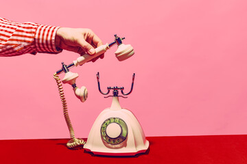 Pop art photography. Retro objects, gadgets. Female hand holding handset of vintage phone isolated on pink and red background. Vintage, retro fashion style