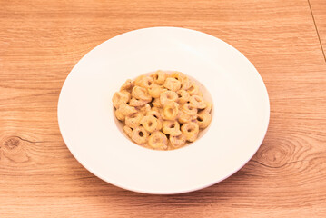 Plate of delicious tortellini in tartufo sauce on white plate and light wood table with knots