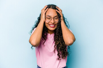 Young hispanic woman isolated on blue background laughs joyfully keeping hands on head. Happiness concept.