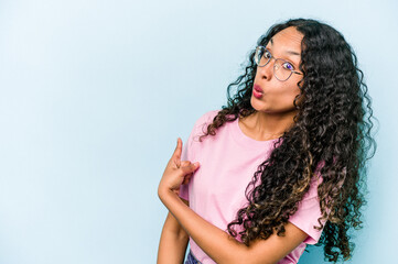 Young hispanic woman isolated on blue background smiling and pointing aside, showing something at blank space.