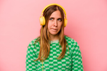 Young caucasian woman listening to music isolated on pink background confused, feels doubtful and unsure.