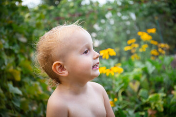 Happy little boy with drops of sweat in  hot weather in summer. Portrait of a smiling toddler staying in a garden.