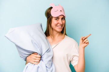 Young caucasian woman wearing a pajama isolated on blue background smiling and pointing aside, showing something at blank space.