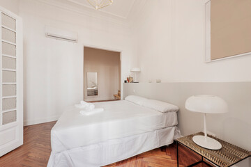 bedroom with double bed, white pillows, dressing room in the background and gray masonry headboard and reddish-colored wooden floors