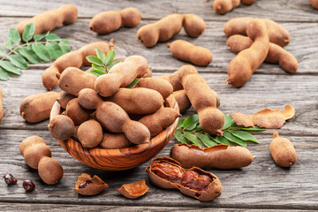Obraz premium Ripe tamarind fruit, leaves and some tamarind seeds on wooden table.